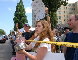 A protester named Marlene, who declined to give her last name, bangs a pot to drown out the singing of Cuba’s national anthem as the country’s interests section becomes an embassy after a 54-year break in diplomatic relations.